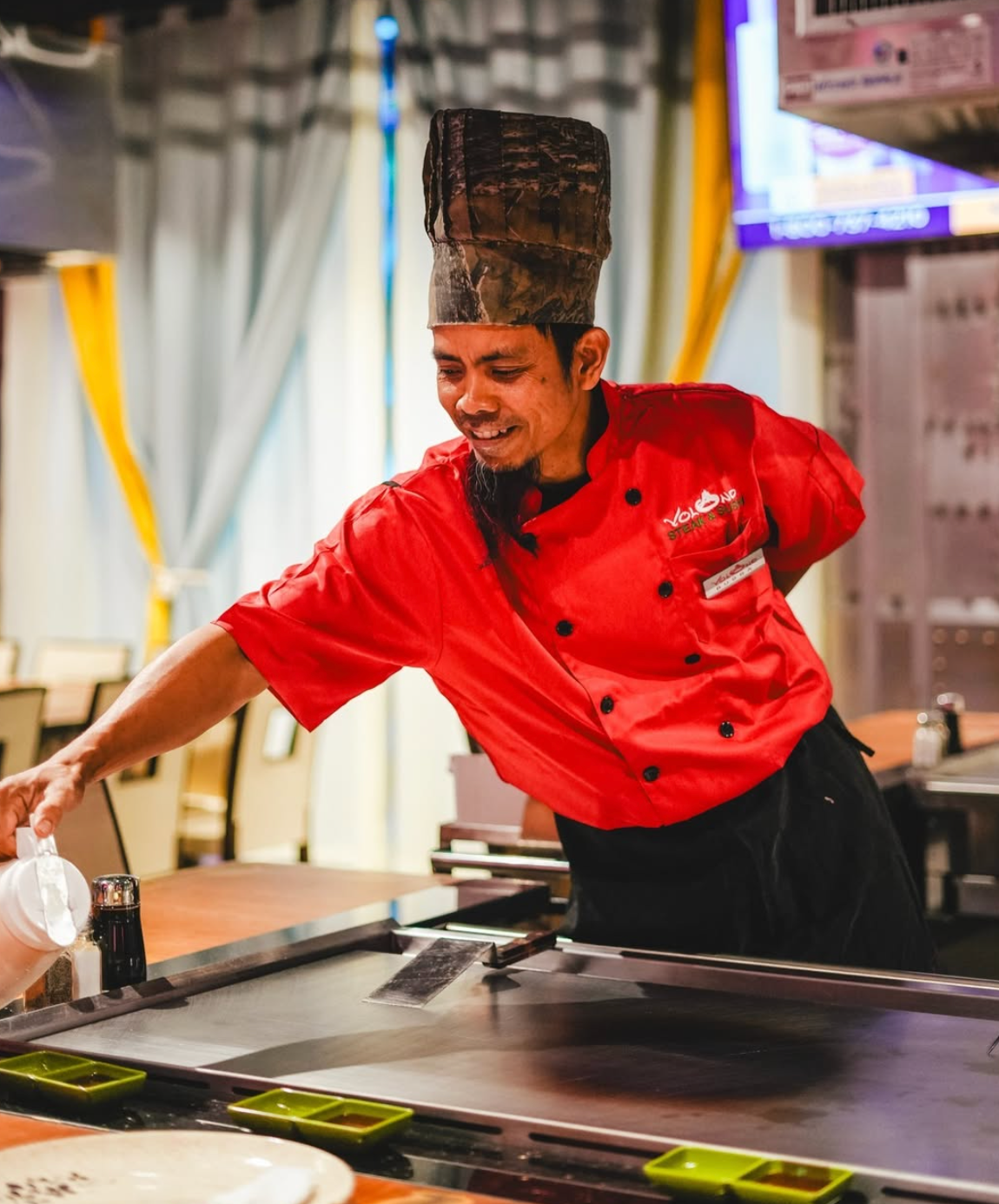 A Volcano hibachi chef in a red uniform preparing food at the grill