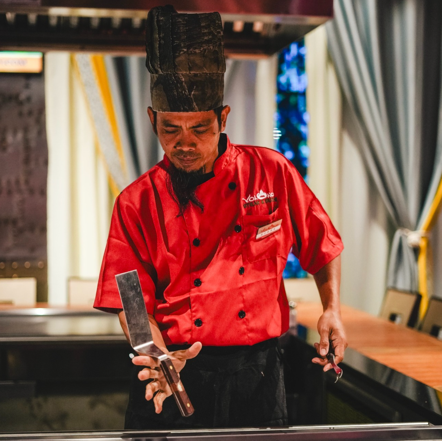 A Volcano hibachi chef working with utensils at the grill